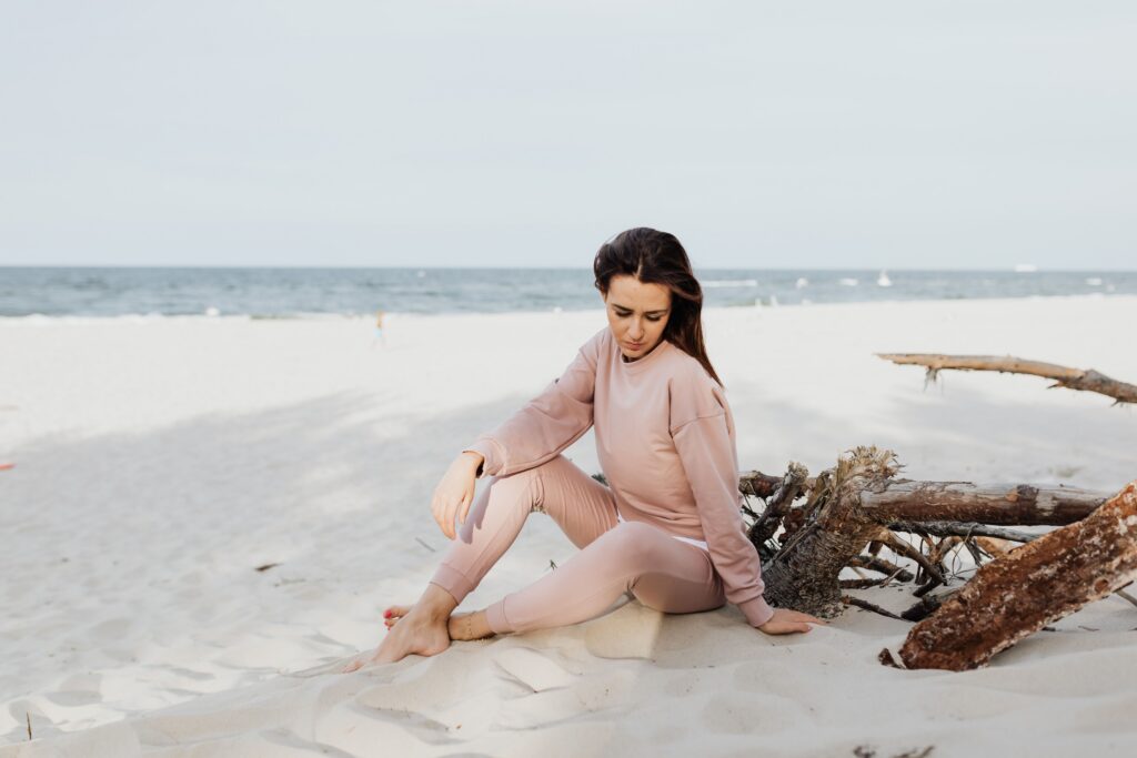 Serene scene of woman pondering alone on a sandy beach in casual pink attire.